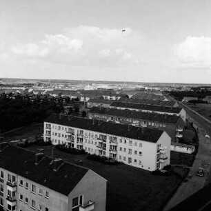 Gartenstadt Falkenberg: Blick vom Rathaus Richtung Nordosten: rechts Stonsdorfer Weg mit parkenden Pkws auf Seitenstreifen: in der Mitte Wohnblocks: dazwischen Grünflächen: links Wäldchen: dahinter Reihenhäuser und weitere Wohnblocks: im Hintergrund das Gewerbegebiet Stonsdorf