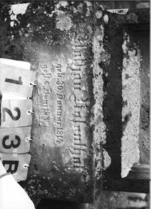 Grabstein 123 (Index: 100114768) Material: Sandstein Zustand: abgeblättert und verwittert mit abgeschrägten Schultern, Voluten und Akroter Maße HxBxT: 141x54x22 cm Beschreibung: Stele auf Sockel, eingezogener Rundbogen mit abgeschrägten Schultern, Voluten und Akroter: Grabstein 123B