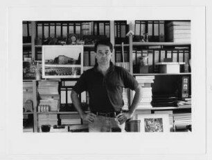 Der Fotograf Karl-Ludwig Lange in seiner Wohnung vor einem Bücherregal mit eigenen Fotografien (u.a. mit der Berliner Mauer)