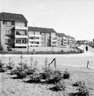 Am Neuen Teich: von links Einmündung Heidekamp: Wohnblocks: mit Balkons: Grünflächen, Jägerzaun, Briefkasten: Frau auf Fußgängerweg, Straßenlampen: im Vordergrund junge Nadelbäume, Zaun: im Hintergrund rechts Einzelhäuser, Garagen, parkende Autos