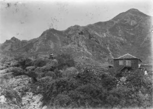 Im Teno-Gebirge : Die Landschaft und Vegetation in der Nähe des Teno-Gebirges. Im rechten Bildrand steht eine Hütte und mittig links sitzt ein Mann auf einem Felsen
