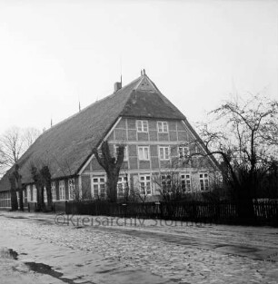 Bauernhaus Ruge/Wömmel: "Bauernvogtei": davor Bäume: rechts Garten hinter Zaun: im Vordergrund Dorfstraße mit Kopfsteinpflaster