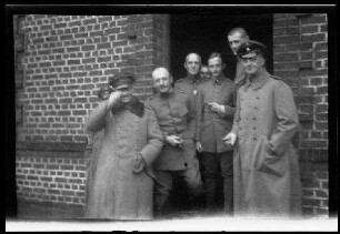 Nicht identifizierbare Ortschaft in Nordfrankreich oder Belgien: 7 Offiziere, 2 davon mit Schirmmütze und Uniformmantel, vor einem Hauseingang (Gruppenbild, Nahaufnahme)