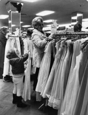 In einem Karstadt-Kaufhaus. Eine Frau steht an einem Warenträger mit festlichen Kleidern. Ihr Kind ist auch schon modeinteressiert