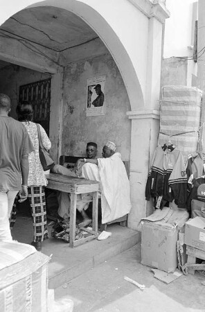 Straßenszene in Serekunda, zwei Männer in einem gewölbten Eingangsbereich sitzend, Gambia