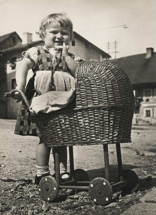 Der kleine Fingerlutscher. Ein kleines Mädchen mit Korbpuppenwagen hat verlegen den Finger im Mund