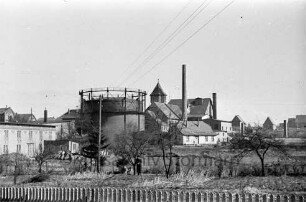 Gaswerk: Lübecker Straße: Blick von Südwesten: mit Gasometer, Kraftwerk, Schornstein: links Tapetenfabrik: rechts Gewächshäuser der Gärtnerei Lichtenberg: Strommast: davor zwei Männer mit Hund: im Vordergrund Lattenzaun