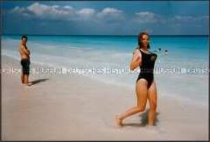 Junge Frau in schwarzem Badeanzug am Strand laufend (Altersgruppe 14-17)