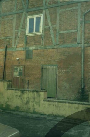 Mühlenplatz 3a: ehemaliger Futtermittelspeicher: Giebelseite: Teilansicht: Erdgeschoss aus Backstein mit Türen, darüber Fachwerk, Fenster, Fallrohr: davor Mauer von Laufgang