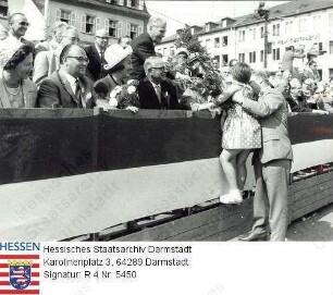 Darmstadt, 1965 Juli 4 / Hessentag, Festzug / Ehrentribüne vor dem Regierungspräsidium mit Gästen des Landkreises Darmstadt, davor stehend: Landrat Gustav Krämer (1909-1991), ein Kind hochhaltend