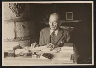Der alte Rudolf Kassner am Schreibtisch mit Büchern und Tintenfässern