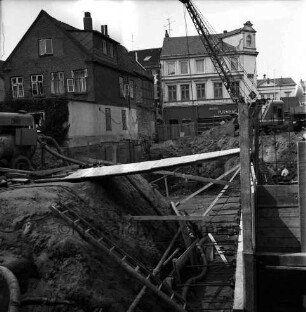 Firma Carl Hoffmann: Hindenburgstraße: Elektrohandel: Neubau: Fundament: Blick in Baugrube mit Holzverschalungen, Brettern, Baumaschine und Bagger: hinten Wohn- und Geschäftshäuser mit Elektrogeschäft Carl Hoffmann und Drogerie Purnhagen: hinten rechts Rathaus