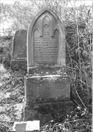 Grabstein 24 (Index: 100114500) Material: Sandstein Zustand: oben beschädigt Maße HxBxT: 158x58x22 cm Beschreibung: Stele, getreppter Sockel, Spitzbogenabschluß, Schriftfeld mit drei türmchenartigen Abschlüssen Symbolik: Blümchen: Grabstein 24