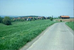 Blick von außen auf Dorf, in das Dorf führende Straße