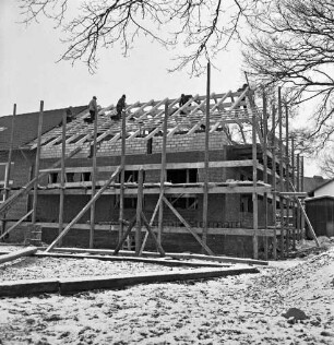 Volkshochschule Barsbüttel-Stellau: Erweiterungsbau: Richtfest: hinten Gebäudeteil mit Gerüsten: im Dachgeschoss zwischen Dachsparren Arbeiter beim Anbringen der Richtkrone: links altes Gebäude: Winter
