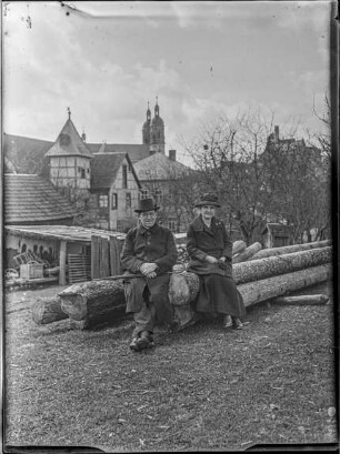 Personen, Käthe und Schorsch auf einem Holzstoß sitzend - im Hintergrund die Basilika und die Burg in Gößweinstein