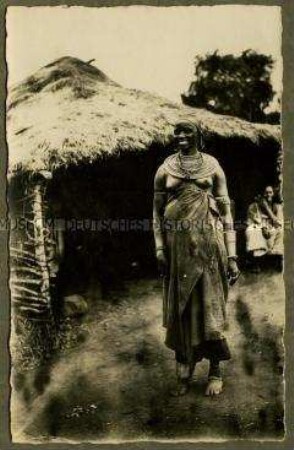 Schwangere Massai-Frau vor einer Hütte