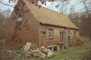 An de Sylsbek 3: traufständige Mehrfamilienkate aus Backstein: Nebengebäude: in Traufseite Türen, vor Hauswand Bank, Stapel mit Feldsteinen, Backsteine: 24. November 1988