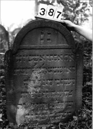 Grabstein 387 (Index: 99803617) Material: Sandstein Zustand: partiell verwittert/Textverlust Maße HxBxT: 89x60x8 cm Beschreibung: Stele mit Karniesbogen, profilierter Rand, Giebelfeld, Seitenakroterien: Grabstein 387