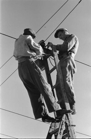 Energieversorgung. Arbeiten an einer Oberleitung. Ansicht mit zwei Arbeitern auf einem Mast