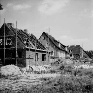 Gartenstraße: Neubaugebiet mit Einfamilienhäusern: vorn links und hinten rechts Rohbauten mit Gerüsten: dazwischen Häuser nach Fertigstellung: vorn Sandhaufen, Baumaterial und Gestrüpp