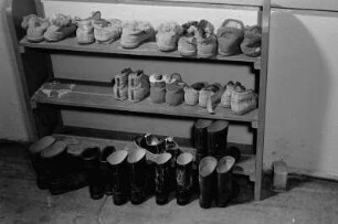 Landflucht. Schuhregal mit Hausschugen und davor abgestellten Gummistiefel (wohl im Lehrlingswohnheim in Trinwillerhagen)