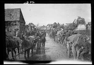 Nicht identifizierbare Ortschaft bei Saint-Quentin (?) (Dep. Aisne, Frankreich): Pferdegespanne mit Soldaten in beiden Richtungen auf einer morastigen Ortsstraße zwischen Gebäuderuinen ("Truppen ziehen durch eine zerstörte Ortschaft")
