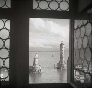 Hafeneinfahrt von Lindau - Harbour entrance of Lindau : Lindau. Blick durch ein Fenster auf die Hafenfahrt mit dem Bayerischen Löwen und dem Neuen Leuchtturm