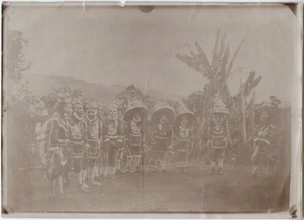 Masked dancers in front of a hut