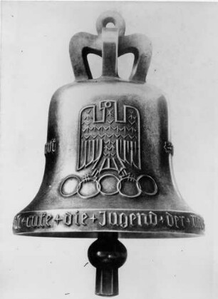Abbildung der Olympia Glocke von 1936 mit der Aufschrift "Ich rufe die Jugend der Welt - Olympische Spiele 1936", dem Reichsadler und den Olympischen Ringen. Die Originalglocke wurde in der ältesten Stahlgießerei der Welt Bochumer Verein für Gußstahlfabrikation Aktiengesellschaft hergestellt und 1936 im Glockenturm des Olympiastadions Berlins aufgehängt. Sie läutete im August 1936 die XI. Olympischen Spiele ein. 1947 zerstört.
