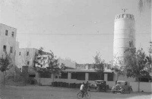 Indisches Viertel in Mogadischu : Blick über eine Straße des indischen Viertels in Mogadischu, auf der ein Radfahrer unterwegs ist. Im Hintergrund erhebt sich ein steinernder Turm. Im Vordergrund zwei Autos.