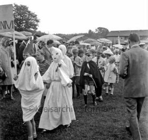 Kindervogelschießen: Festwiese: Festumzug: Schulkinder in Kostümen als Gespenster und Piraten: dahinter Zuschauer mit Regenschirmen: vorn rechts Mann: hinten Wohnblock und Bäume