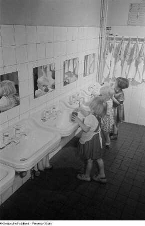 Drei Kleinkinder an Waschbecken eines Kinderkrippenbaderaums beim Zähneputzen