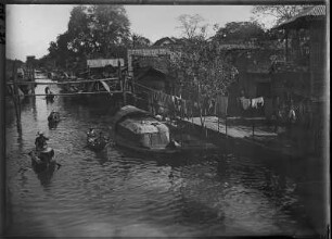 Leben am Fluss : Phetchaburi. Blick auf den von Häusern gesäumten Fluss mit Booten, 1909/1910