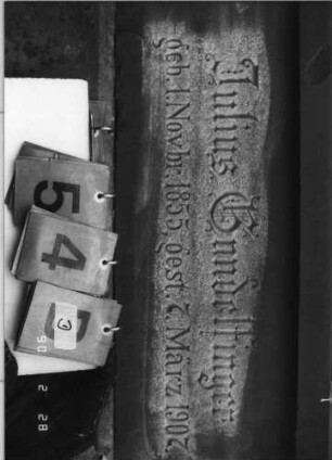 Grabstein 54 (Index: 100114898) Material: Sandstein und polierter Granit Zustand: Stele verrutscht, Texttafel mehrfach zerbrochen und repariert Maße HxBxT: 263x71x36 cm Beschreibung: Ädikula mit gestuftem Sockel auf Rustikasockel, eingezogener Spitzgiebel mit Akroteren und Laubdekor, eingesetzte Texttafel: Grabstein 54D
