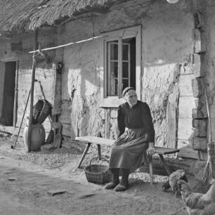 Strohgedecktes Blockhaus in Burg-Kauper. Frau Nowick in Spreewälder Alltagstracht vor ihrem Gehöft. : Ze słomu skryte kładźity twar statoka w Kupaŕskich Bórkowach. Knjeni Nowickowa we wšědnej Błótowskej drasće před swojim statokom.