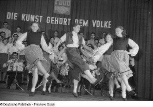 Tanzende Paare, im Hintergrund Chor und Orchester beim Kreisausscheid für Volkskunst