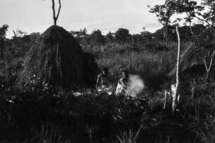 Lundafrauen : Zwei Frauen der Lunda an einem Feuer vor einer Grashütte. Dahinter eine verwilderte Rodung.
