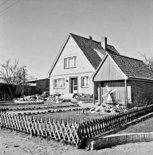 Neubausiedlung: Einfamilienhaus mit Garage: davor geschmückter Vorgarten mit Jägerzaun: links Baum: vorn rechts Modellwindmühle