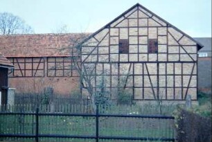 Blick über Zaun und Nutzgarten auf eine große Fachwerkscheune