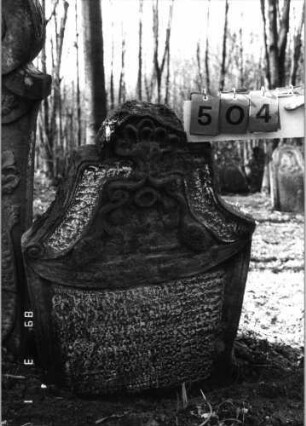 Grabstein 504 (Index: 99752922) Material: Sandstein Zustand: stark verwitt. mit fast völl. Textverlust Maße HxBxT: 117x68x11 cm Beschreibung: Stele, in Voluten auslaufender eingezog. Rundbogenabschl. Symbolik: zwei Trauben, Voluten, Muschel: Grabstein 504
