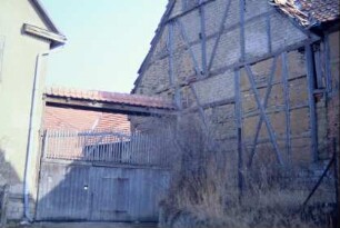 Eingangsbereich zu einem Gehöft; überdachtes zweiflügeliges Holztor; rechts Wirtschaftsgebäude