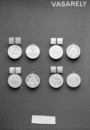 Vier Medaillen der Deutschen Demokratischen Republik (DDR). Oben: Medaille für hervorragende Leistungen in der Leicht-, Lebensmittel- und Nahrungsgüterindustrie der DDR (vergoldet; 30 mm Durchmesser; 1975 gestiftet) an Spange (rosa bezogen; 12,5 x 25 mm) und Medaille für hervorragende Leistungen im Handel der DDR (vergoldet; 30 mm Durchmesser; 1975 gestiftet) an Spange (weiß bezogen; 13 x 25 mm). Jeweils Avers und Revers mit Staatswappen (ohne Spange). Unten: Medaille für hervorragende Leistungen in der chemischen Industrie der DDR (vergoldet; 30 mm Durchmesser; 1975 gestiftet) an Spange (gelb bezogen; 12,5 x 25 mm) und Medaille für hervorragende Leistungen in der Metallurgie der DDR (vergoldet; 30 mm Durchmesser; 1975 gestiftet) an Spange (orangefarben bezogen; 12,5 x 25 mm). Jeweils Avers und Revers mit Staatswappen (ohne Spange)