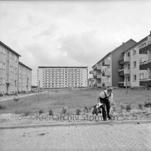 Klosterbergen: Bogenstraße: rechts und links dreigeschossige Wohnblocks: in der Mitte Grünanlage mit Wäschestangen: vorn rechts Mann mit Kind und Plastikauto: hinten Mitte achtgeschossiges Punkthaus nach Fertigstellung