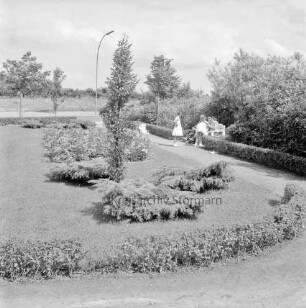 Grünanlage am Berliner Ring: vorn Rasenfläche mit Baum und Sträuchern: hinten rechts Bank: darauf Personen: davor Mädchen und Kinderwagen
