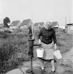 Wohnungsbau: Wohngebiet Kellerberg-Süd: Frau an Wasserpumpe: dahinter Schuppen: rechts "Steinbaracke": im Hintergrund Einfamilienhäuser