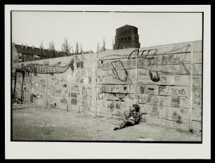 Ein Mädchen an der Berliner Mauer sitzend, mit Blick auf den Kirchturm der Pfarrkirche Heilige Familie, Prenzlauer Berg, Berlin