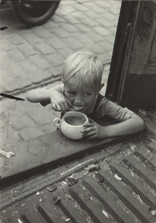 Kind beim Löffeln einer Suppe an der Laderampe eines Transportfahrzeugs. Das Foto wurde in einem beschädigten Straßenbahnfahrzeug vor dem Bahnhof Hamburg-Altona am Montag, 26. Juli 1943 während der Aktion "Gomorrha" aufgenommen