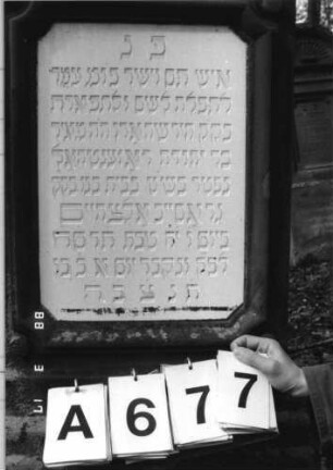 Grabstein 677 (Index: 99901927) Material: Sandstein und weiße Glasplatten Maße HxBxT: 162x53x25 cm Besonderheit: kulturhistorisch wertvoll / hist.-wiss. Gründe (Gemeindestellung): Grabstein 677A