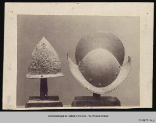 Zwei Helme: Ein konischer Eisenhut mit mythologischen Darstellungen und ein mit wenigen floralen Ornamenten verzierter Morion mit hohem Helmkamm